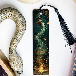 May include: A green and gold bookmark with a swirling design and the text "SPELLBOOK". The bookmark has a black tassel.