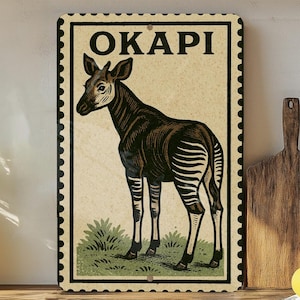 May include: Vintage-style metal sign featuring an okapi illustration. The sign has a cream-colored background with the word "OKAPI" at the top. The okapi is depicted in brown and white, standing on green grass. The sign has a black border.