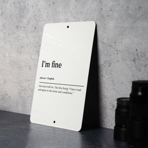 May include: White metal sign with black text that reads "I'm fine" and "phrase - English". The text below reads "2nd most told lie. The first being "I have read and agree to the terms and conditions."