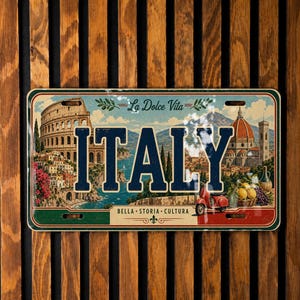 May include: A rectangular metal sign featuring the word ITALY in large blue letters. The design includes illustrations of the Colosseum, a cathedral, a red scooter, and lemons. The text La Dolce Vita and BELLA STORIA CULTURA are printed on the sign.