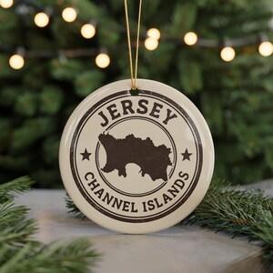 A circular ornament with the text "JERSEY CHANNEL ISLANDS" and a silhouette of Jersey, a small island in the Channel Islands, is displayed in front of a Christmas tree with twinkling lights.