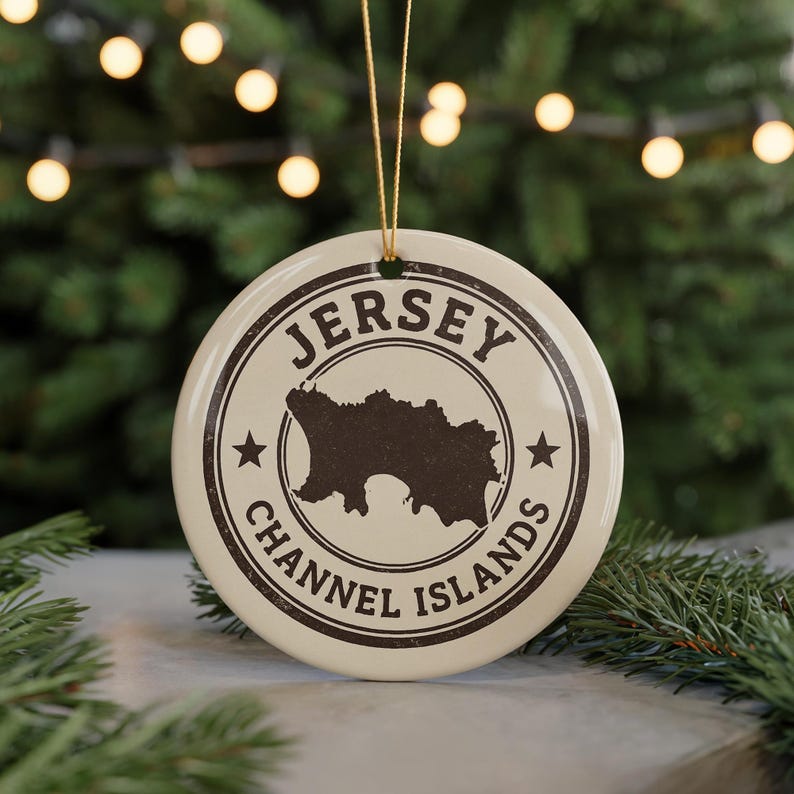 A circular ornament with the text "JERSEY CHANNEL ISLANDS" and a silhouette of Jersey, a small island in the Channel Islands, is displayed in front of a Christmas tree with twinkling lights.