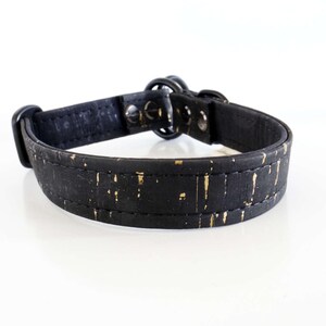 May include: A black dog collar with gold flecks. The collar is made of a textured material and features a metal buckle and hardware. The collar is designed for a pet.