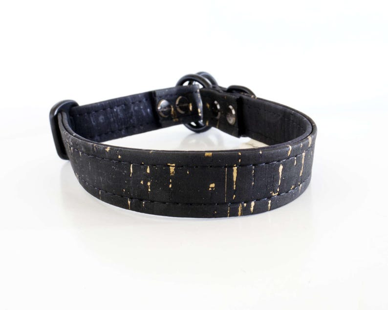May include: A black dog collar with gold flecks. The collar is made of a textured material and features a metal buckle and hardware. The collar is designed for a pet.