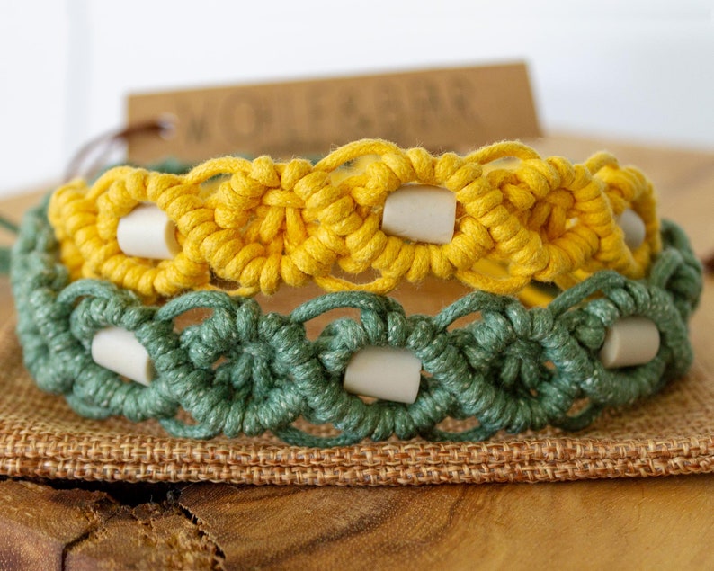 May include: Two macrame bracelets, one yellow and one green, are stacked. Each bracelet features a woven design with white cylindrical beads. The bracelets are displayed on a burlap surface.