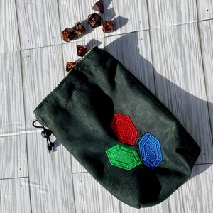 May include: A black drawstring bag with a red, green, and blue embroidered design of three gemstones. The bag is filled with brown dice.