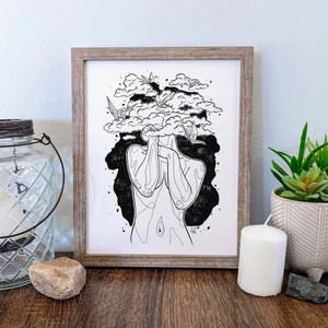 May include: Black and white line art print of a person with clouds and origami birds covering their head. The print is framed in a light brown wood frame.