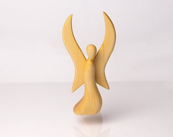 Puede incluir: Una figurita de ángel de madera con las alas extendidas. El ángel está tallado en madera clara y tiene un diseño simple y elegante.
