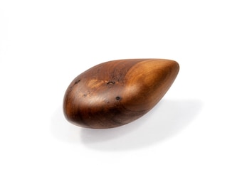 Puede incluir: Un objeto de madera liso con forma de lágrima de color marrón oscuro. La madera tiene un veteado natural y un acabado ligeramente brillante.
