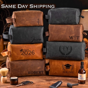 May include: A collection of personalized leather toiletry bags in various shades of brown and black. Some bags feature names, initials, or graduation year and class details. Accessories like a shaving brush, scissors, and a bottle are also present.