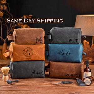 May include: Six rectangular toiletry bags in brown, gray, and blue leather-like material, each featuring unique personalized engravings. The bags are stacked in two columns, accompanied by a shaving brush, a razor, a small bottle, and a jar.