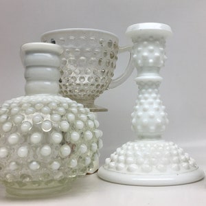 May include: Four white milk glass items, including a jug, a bottle, a cup, and a candle holder, all with a textured, raised dot pattern.