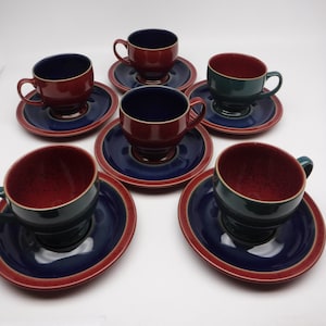 May include: Set of six red and green teacups and saucers with a blue and red rim. The cups and saucers have a speckled glaze.