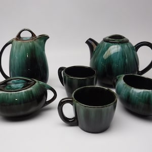 May include: A green and black ceramic tea set with a teapot, creamer, sugar bowl, and two cups.