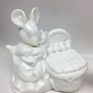May include: White porcelain figurine of a mouse holding a baby mouse in a basket. The mouse is sitting on a rock and the basket is filled with small white balls.