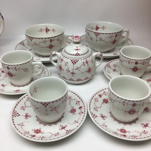 Puede incluir: Un juego de té vintage con un patrón floral rojo. El juego incluye una tetera, un azucarero, una jarra de crema y cuatro tazas y platillos.