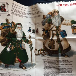 Könnte beinhalten: Stoffpaneel mit zwei Illustrationen von viktorianischen Weihnachtsmännern, einer in einem grünen Mantel, der andere in einem beigen Mantel, beide mit langen weißen Bärten. Der Text "OLDE FATHER CHRISTMAS APPLIQUE" ist sichtbar.