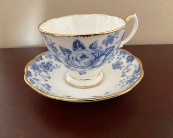 May include: A white teacup and saucer with a blue and gold floral pattern. The cup has a handle and the saucer has a scalloped edge.