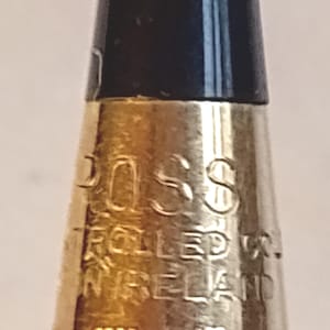 Könnte beinhalten: Nahaufnahme eines goldfarbenen Stifts mit schwarzer Spitze. Der Stift trägt die Gravur "CROSS" sowie "ROLLED" und "IN IRELAND". Der Stift ist ein Schreibgerät.