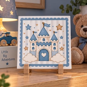 Può includere: Una piastrella quadrata in ceramica con un'illustrazione stravagante di un castello azzurro e beige con una porta a forma di cuore, circondato da nuvole e stelle, racchiuso in un bordo blu smerlato, esposto su un piccolo supporto in legno.