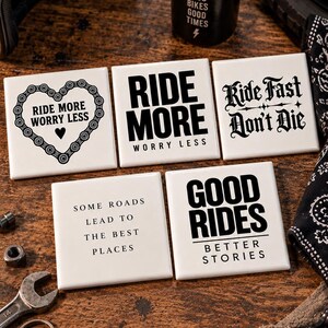 May include: Five square white ceramic coasters featuring black text and graphics. Designs include a motorcycle chain heart with "RIDE MORE WORRY LESS," "RIDE MORE WORRY LESS," "Ride Fast Don't Die," "SOME ROADS LEAD TO THE BEST PLACES," and "GOOD RIDES BETTER STORIES."