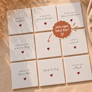 Puede incluir: Un conjunto de nueve azulejos de cerámica blancos cuadrados dispuestos en cuadrícula, cada uno con un pequeño corazón rojo y texto en neerlandés como Huisje vol liefde, Jij bent mijn lievelings y Geniet van de kleine dingen, con una etiqueta marrón.
