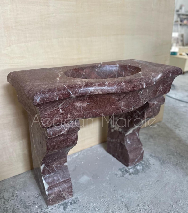 May include: A red marble bathroom vanity with a curved top and a sink. The vanity has two legs with ornate details.