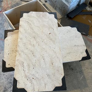 Può includere: Tre piastrelle rettangolari in pietra beige chiaro con angoli grigio scuro. Le piastrelle hanno una superficie strutturata e sono disposte a strati. Sembrano far parte di un progetto di costruzione più ampio.