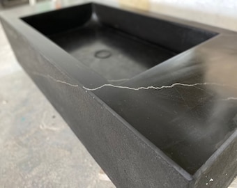 May include: A black rectangular concrete sink with a white vein running through it. The sink has a square, recessed basin.