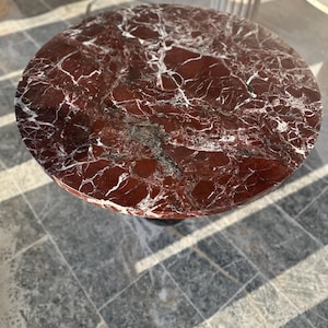 Pode incluir: Um tampo de mesa redondo de mármore vermelho com veios brancos. O tampo da mesa é liso e polido.
