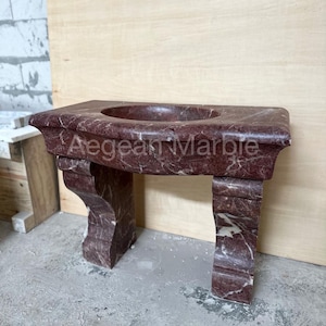 May include: A red marble bathroom vanity with a curved top and two legs. The vanity is made of a natural stone with a unique veining pattern.