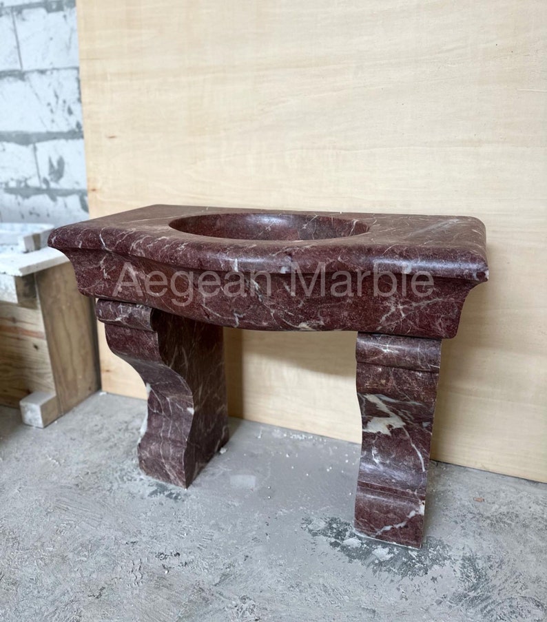 May include: A red marble bathroom vanity with a curved top and two legs. The vanity is made of a natural stone with a unique veining pattern.