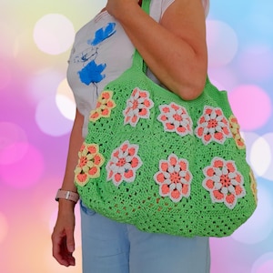 May include: A green crocheted tote bag with colourful flower designs. The bag has a wide, open top and is made with a thick, textured yarn.