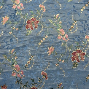 May include: Blue fabric with a floral pattern. The flowers are pink, red, and gold. The fabric has a subtle texture.