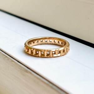 May include: A gold band ring with a geometric design and the inscription "Tiffany & Co. Au750 Italy".