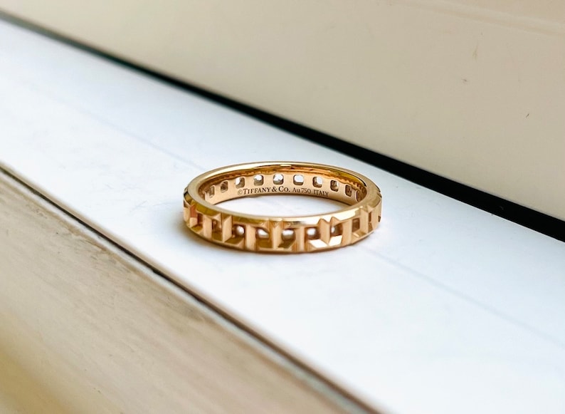 May include: A gold band ring with a geometric design and the inscription "Tiffany & Co. Au750 Italy".