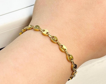 Könnte beinhalten: Ein goldenes Kettenarmband mit einem Gliederdesign. Das Armband befindet sich an einem Handgelenk.