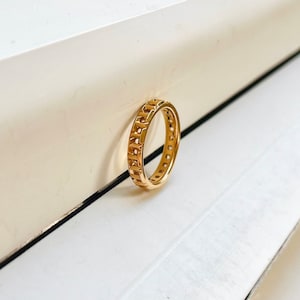 May include: A gold ring with a geometric design. The ring is made of a thick band with a repeating pattern of squares and circles.