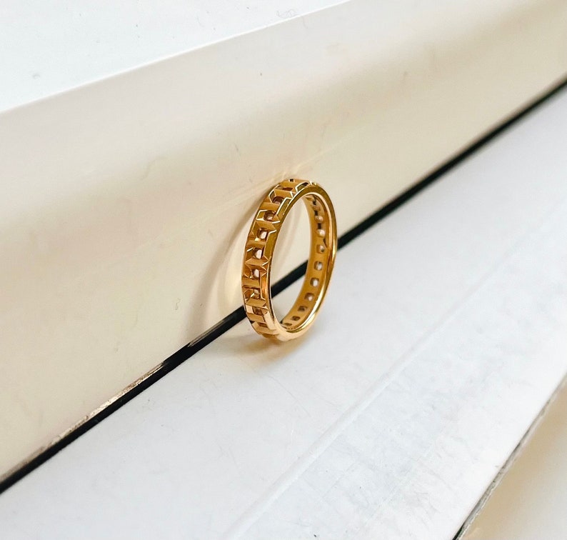 May include: A gold ring with a geometric design. The ring is made of a thick band with a repeating pattern of squares and circles.