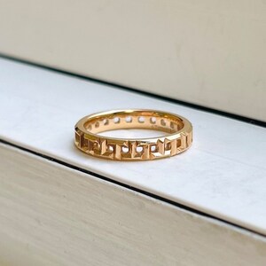 May include: A gold band ring with a geometric design. The ring is made of a smooth, polished metal and has a simple, elegant style.