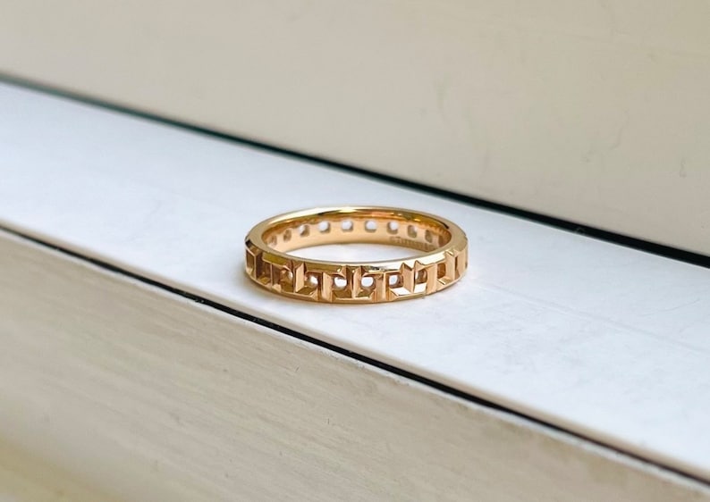 May include: A gold band ring with a geometric design. The ring is made of a smooth, polished metal and has a simple, elegant style.