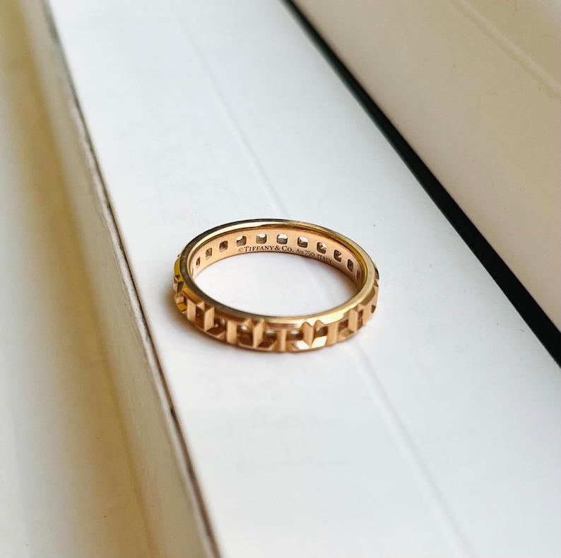 May include: A gold band ring with a geometric design and the inscription "Tiffany & Co. AG 925 ITALY".