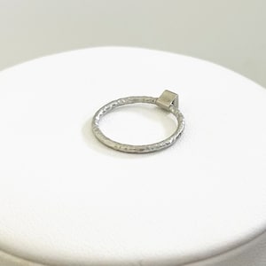May include: A silver ring with a textured band and a square-shaped stone.