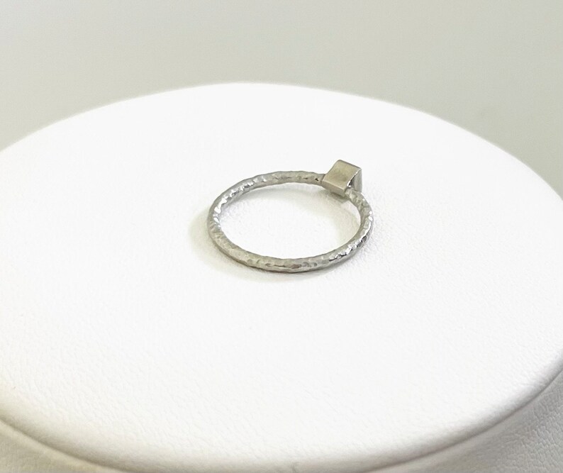 May include: A silver ring with a textured band and a square-shaped stone.