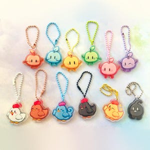 May include: A collection of colorful acrylic keychains featuring cartoon fruit and bird designs. The keychains have metal ball chains and lobster claw clasps. The fruit designs include apples and the bird designs include chickens and ducks.