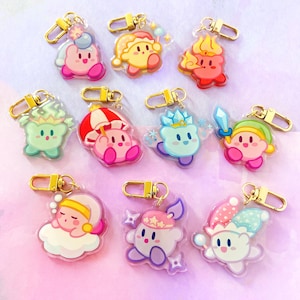May include: A collection of colorful acrylic keychains featuring various character designs. Each keychain has a gold-colored clasp. The characters are in various poses and outfits, with pink, yellow, blue, and green being the dominant colors.