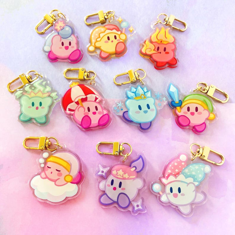 May include: A collection of colorful acrylic keychains featuring various character designs. Each keychain has a gold-colored clasp. The characters are in various poses and outfits, with pink, yellow, blue, and green being the dominant colors.