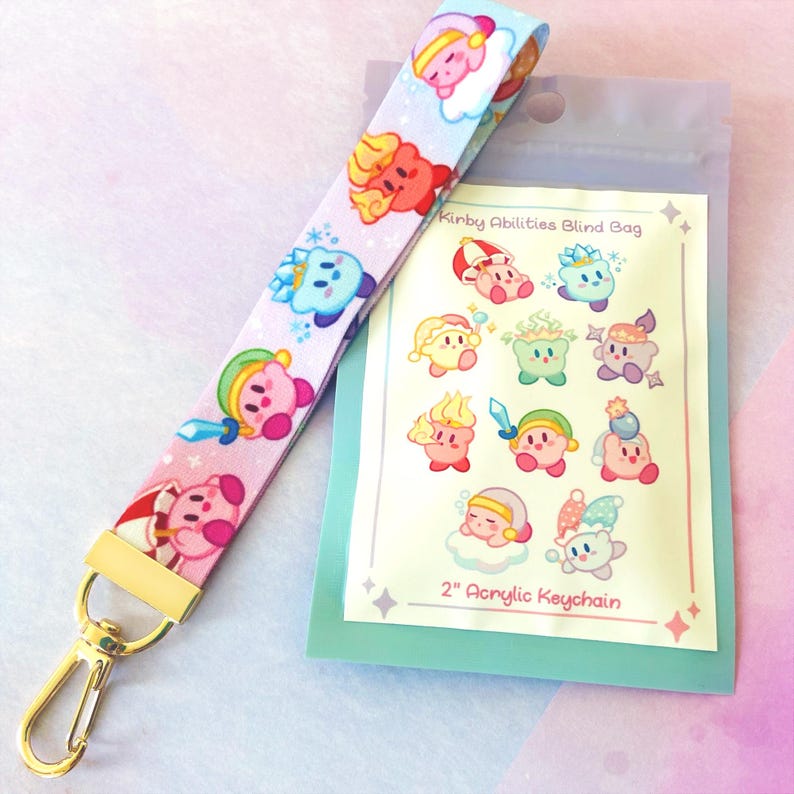 May include: A pink and white lanyard with cartoon character designs and a gold-colored clasp. The lanyard features various character illustrations. A small, clear bag with a 2" acrylic keychain is also visible.