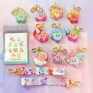 May include: A collection of colorful acrylic keychains featuring various character designs. The keychains have gold-colored clasps. Also included are two matching lanyards and a blind bag with the text "Kirby Abilities Blind Bag" and "2" Acrylic Keychain".