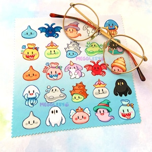 May include: A light blue microfiber cleaning cloth featuring a repeating pattern of colorful cartoon monsters and the text "MEGGLESY". Gold-rimmed eyeglasses rest on the cloth.